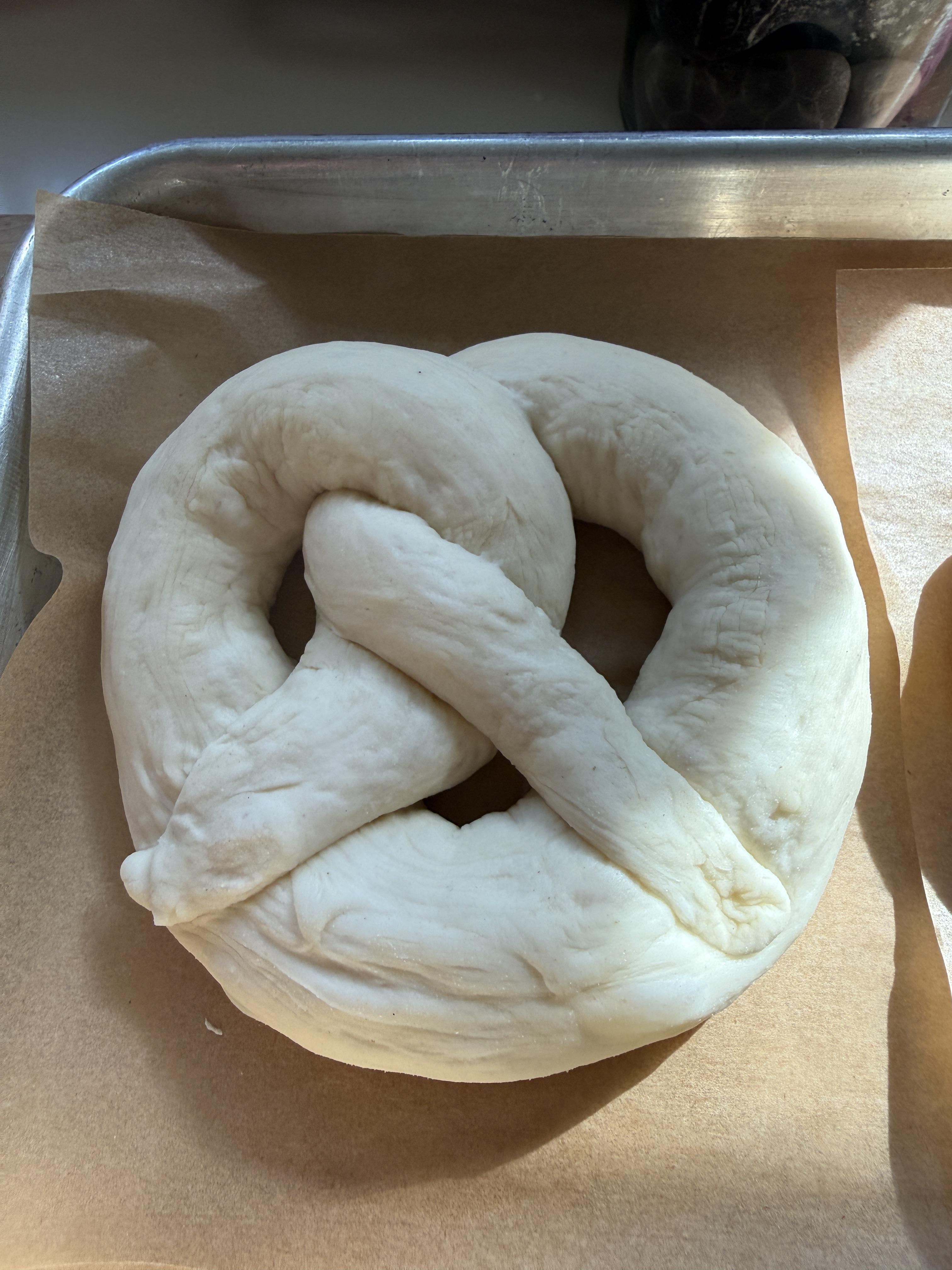 A single raw shaped pretzel on parchment, classic braid, the moment before the bath
